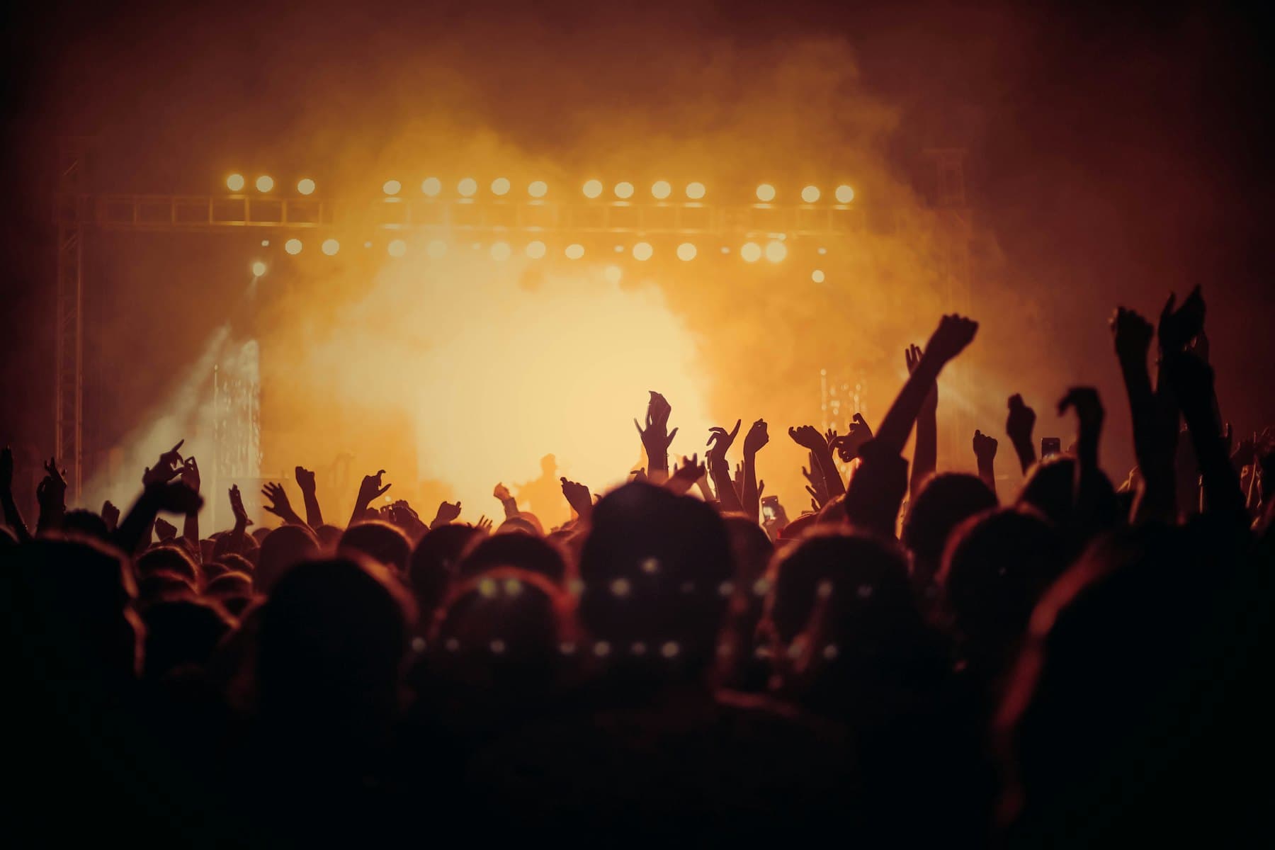 Crowd with raised hands silhouetted against warm stage light